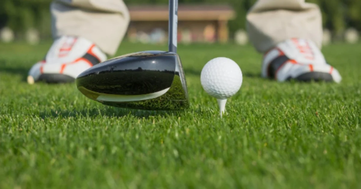 A golf driver positioned behind a ball on a tee, ready for a swing on manicured grass.